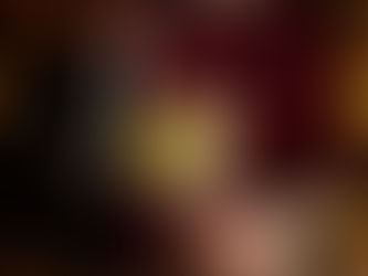 A bartender in a red plaid shirt pours sparkling water from a silver soda siphon into a large glass filled with ice and a lime wheel in a dimly lit bar.