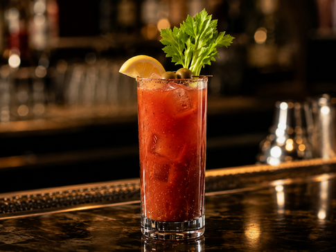 An elegant Bloody Mary in a tall highball glass on a dark wood bar, garnished with a single short celery stalk and a thin lemon wheel.