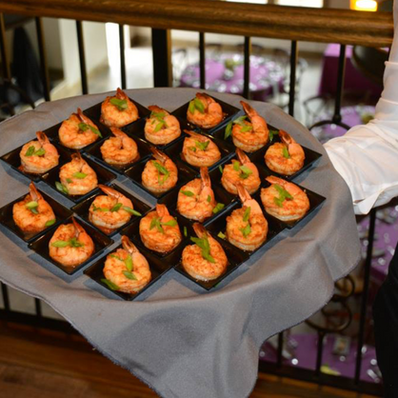 Server holding a tray of grilled shrimp appetizers with green onions.