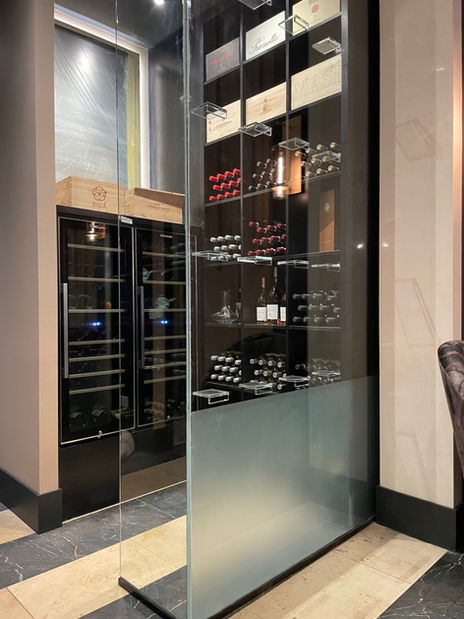 Full-height custom glass wine display enclosure with metal shelving and smoked glass installed by Hurry Bros.
