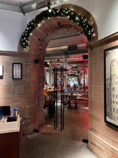 Frameless toughened glass doors installed within arched stone opening in hospitality space by Hurry Bros.