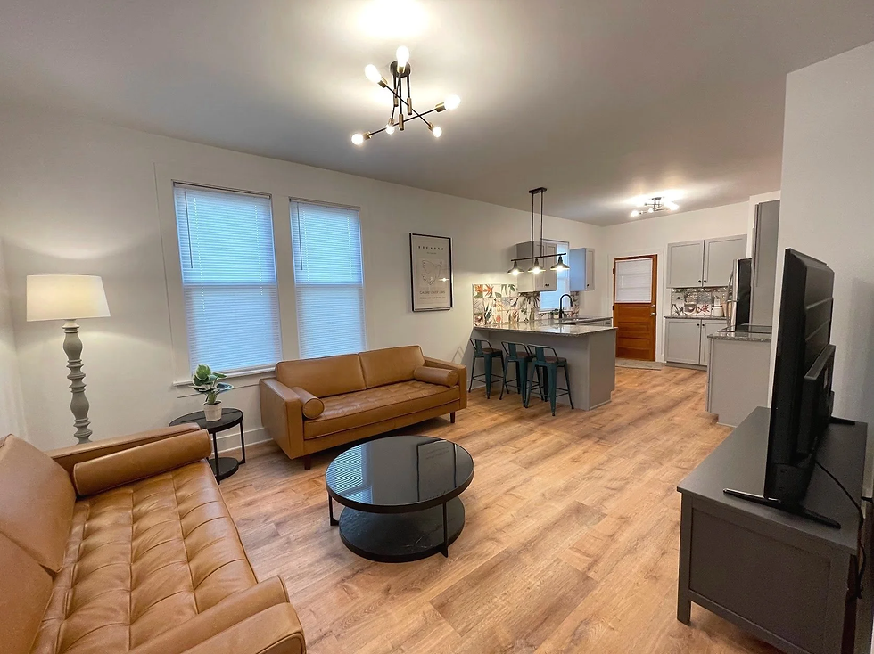 Spacious, bright open-concept student apartment living room and kitchen in a RentBing downtown Binghamton property. Features plush leather sofas, large windows, modern kitchen island, and hardwood floors — perfect for independent living without roommates.