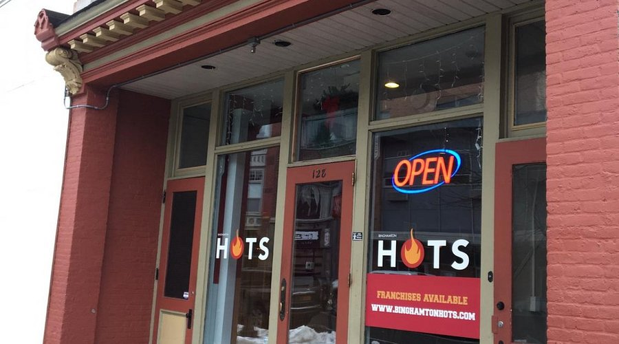 Red brick storefront with sign "HOTS," neon "OPEN." Red and beige doors, snow on sidewalk. Text: Franchises Available, website listed.