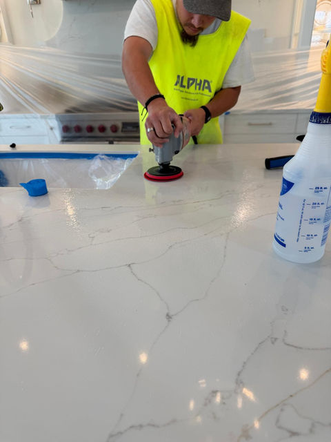 Man in ALPHA vest polishing white kitchen countertop with power tool.