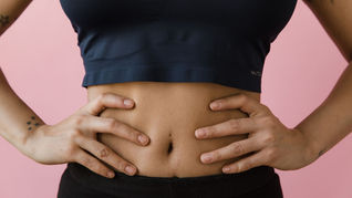 A person in athletic wear places their hands on their waist, highlighting a focus on fitness and core strength against a pink background.