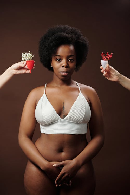 Black woman with her hands over her lower stomach. 2 diva cups are being held by hands on either side of her head