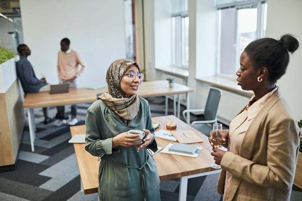 2 women holding drinks and talking to each other. 2 men are also talking to each other in the background