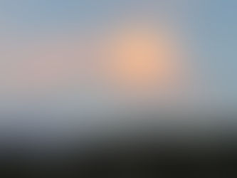 A pink and purple cloud hovering over the hillside at dusk. 