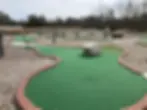 Completed 18-hole mini golf course with curved artificial turf greens, brick borders, decorative boulders, and gravel pathways.
