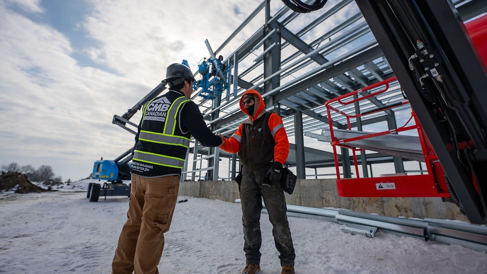 Two construction professionals shake hands on a winter jobsite beside a steel building frame, representing trusted partnerships and on-site collaboration.
