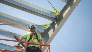 Construction worker in a safety harness installing the high-performance DonoBrace tension rod bracing system onto structural steel I-beams.