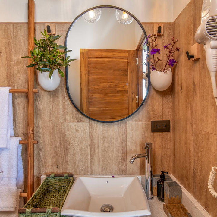 Eco-friendly bathroom vanity with wood-look panels, round mirror, and green wicker decor in a Monteverde Airbnb — designed by Decor Online by Vane.