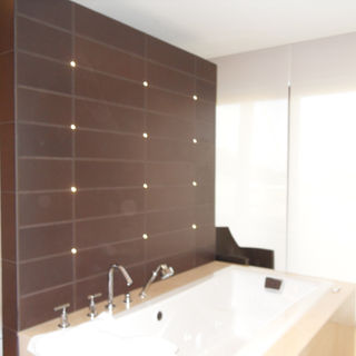Baño moderno con pared divisoria enchapado en porcelanato oscuro  con luz empotrada y tina moderna empotrada 