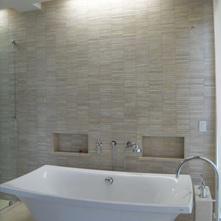 Baño moderno con nichos con enchapes de pared a pared en mármol blanco beige con una bañera independiente y accesorios para baño marca Kohler e iluminación empotrada