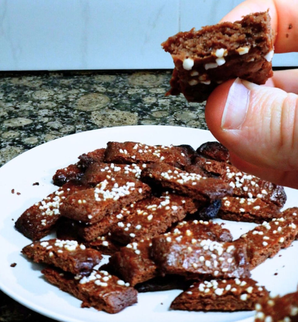 Foto de un plato lleno de galletas, y una mano mostrando una galleta partida por la mitad
