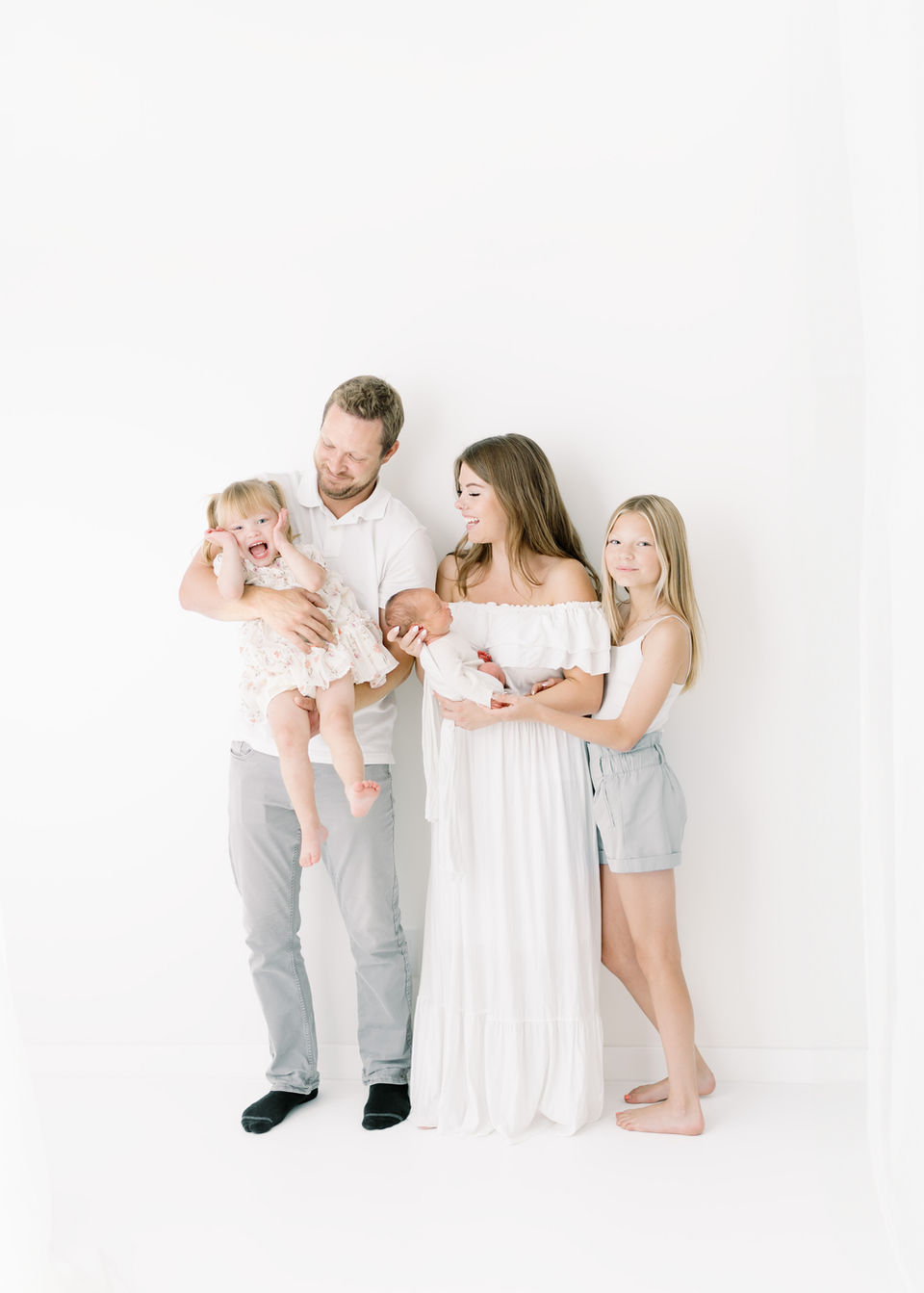 A young family look at their toddler daughter who smiles at the camera.