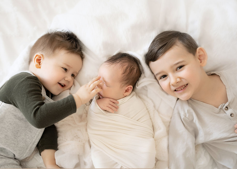 A toddler tickles his 3 week old baby brothers nose while their older brother smiles at the camera at babies Newborn Photography Session.