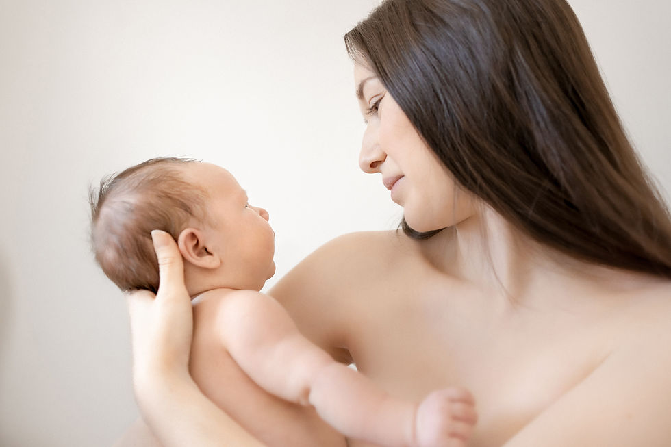 A mother smiles at her baby who stares up at her while they have skin on skin time.