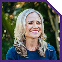 Outdoor headshot of a smiling woman with shoulder-length curly blonde hair