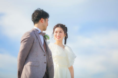 青空を背景に微笑む新郎新婦、名古屋での前撮りの一コマ