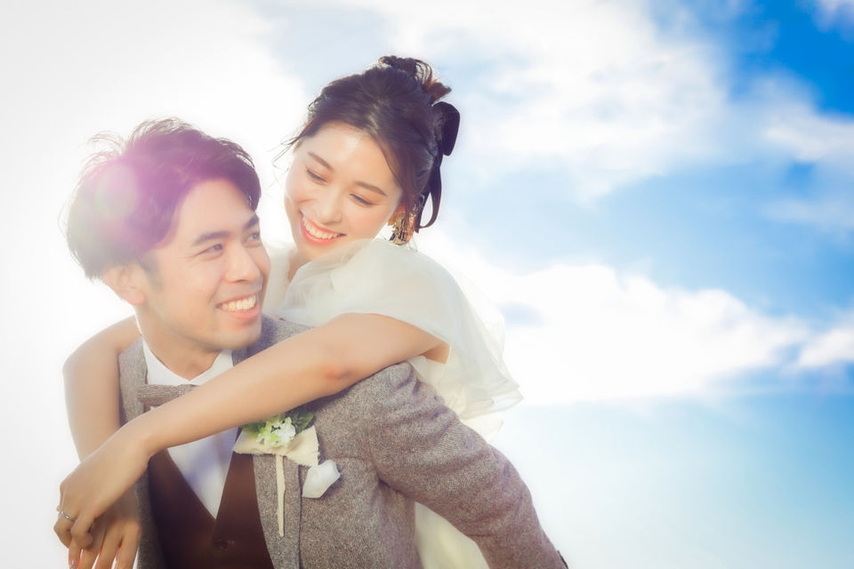 青空の下、新郎に背負われる新婦、名古屋でのフォトウェディングのワンシーン