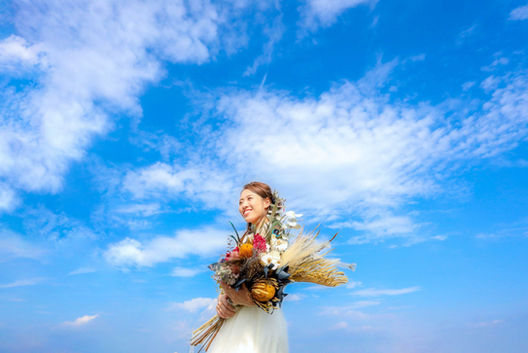 晴れ渡る青空の下、庄内緑地公園で豊かなブーケを抱え微笑む新婦の前撮りショット