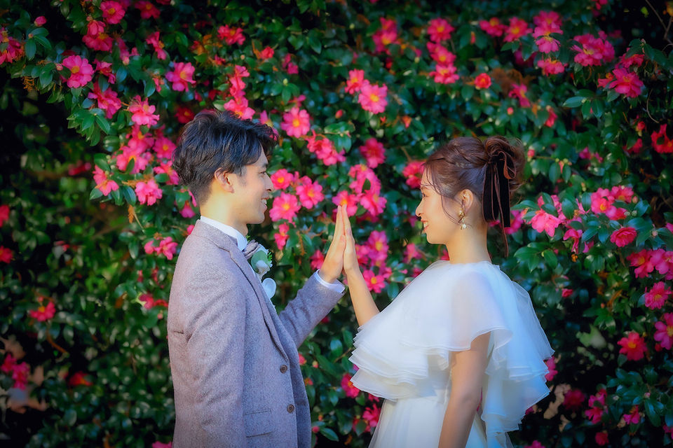花に囲まれた背景で手を合わせる新郎新婦、名古屋でのフォトウェディングのワンシーン