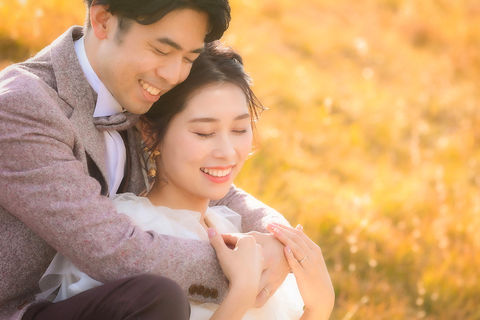 秋の名古屋で草原に座り寄り添う新郎新婦、前撮りの一コマ