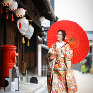 名古屋・古都の街並みで和装前撮りを行う花嫁。色とりどりの打掛と赤い番傘が映えるフォトウェディングショット。
