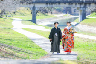 和装で手をつなぎ岡崎公園の小道を歩むカップル、春の陽光と緑の草原を背景に