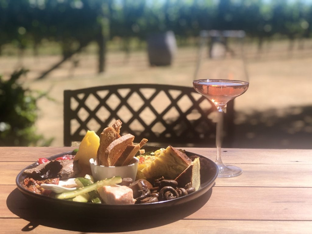 Glass of Rose sitting beside a platter of food