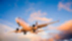 A commercial aeroplane soars through the vibrant sky as the sun sets, casting orange and pink hues on the clouds.