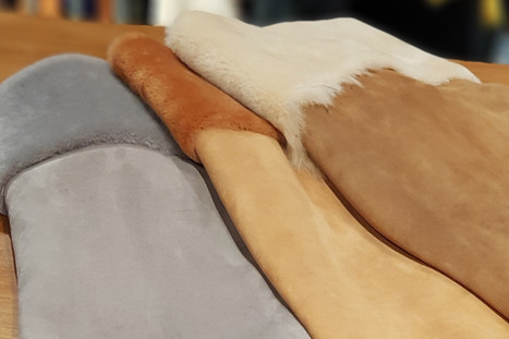 A selection of sheepskin hides in different shades of brown, grey, and white laid out on a wooden table.