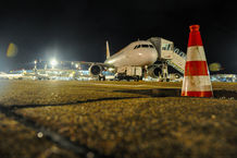 Nachtaufnahme eines Flugzeugs am Flughafen mit einem Verkehrshindernis-Kegel im Vordergrund