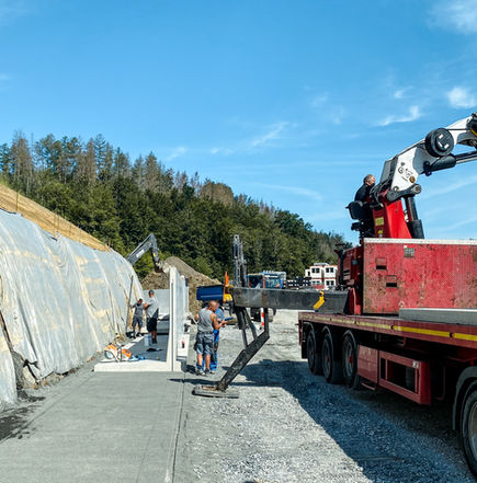 Montage von Betonfertigteilen im Tiefbau mit Kran und Bauarbeitern auf einer Infrastrukturbaustelle