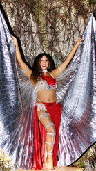 Big silver Isis wings are used as a prop in a photo shoot of Aliza Shoshana. She wears a red sparkly costume.