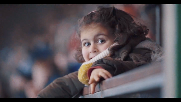 Heureuse enfant souriante en veste et écharpe, se penchant d'une rambarde.