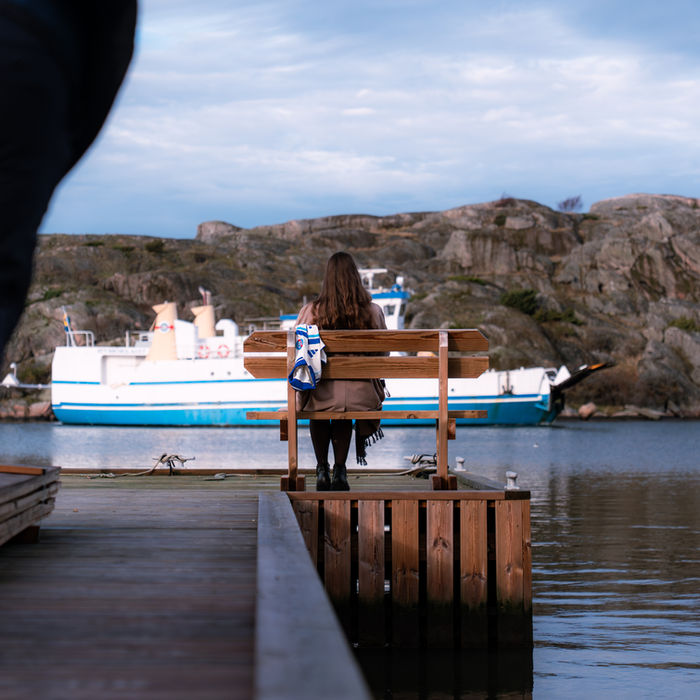 Femme assise sur un banc regardant un ferry blanc et bleu dans un port.