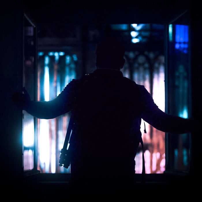 Silhouette d'homme dans l'embrasure, devant des vitraux colorés et lumineux.