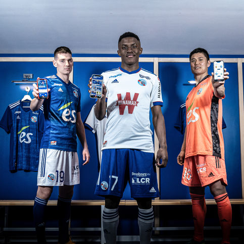 Trois joueurs du RCSA en maillots "es" et "W" présentant téléphones.