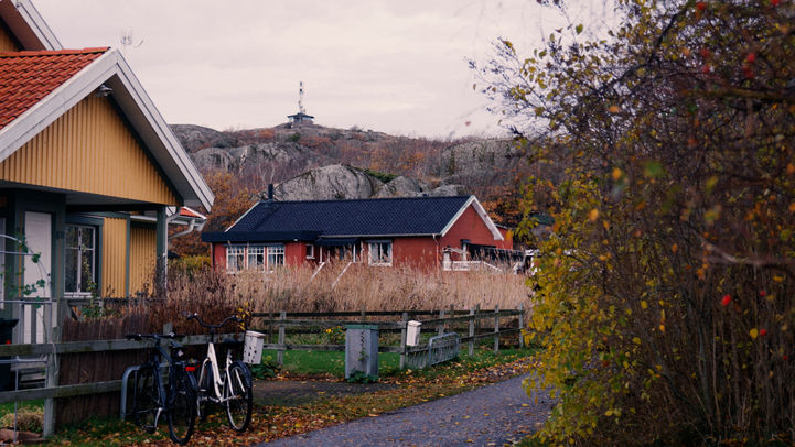 Maisons colorées, vélos garés, chemin et colline rocheuse sous ciel couvert.