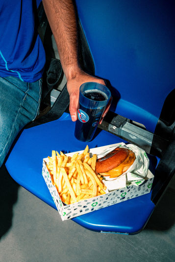 Main tenant une boisson, frites et burger sur plateau bleu.