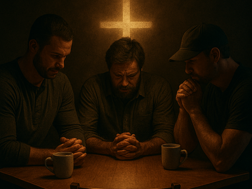 Three men sit in prayer around a wooden table in a dimly lit coffee shop, with an empty chair and a glowing cross on the wall behind them. Bold text reads "REAL MEN SHOW UP."