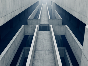 A brutalist concrete corridor viewed from ground level, the path fragmenting into parallel voids that recede toward a distant light with no clear way through.
