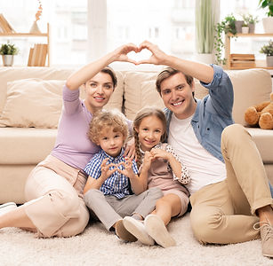happy-parents-two-adorable-siblings-sitting-floor-by-couch-front-camera-making-heart-shape