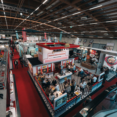 Blick von oben auf die belebten Messehallen der “Alles für den Gast” 2024 im Messezentrum Salzburg. Im Vordergrund der Stand von McCain Foods.