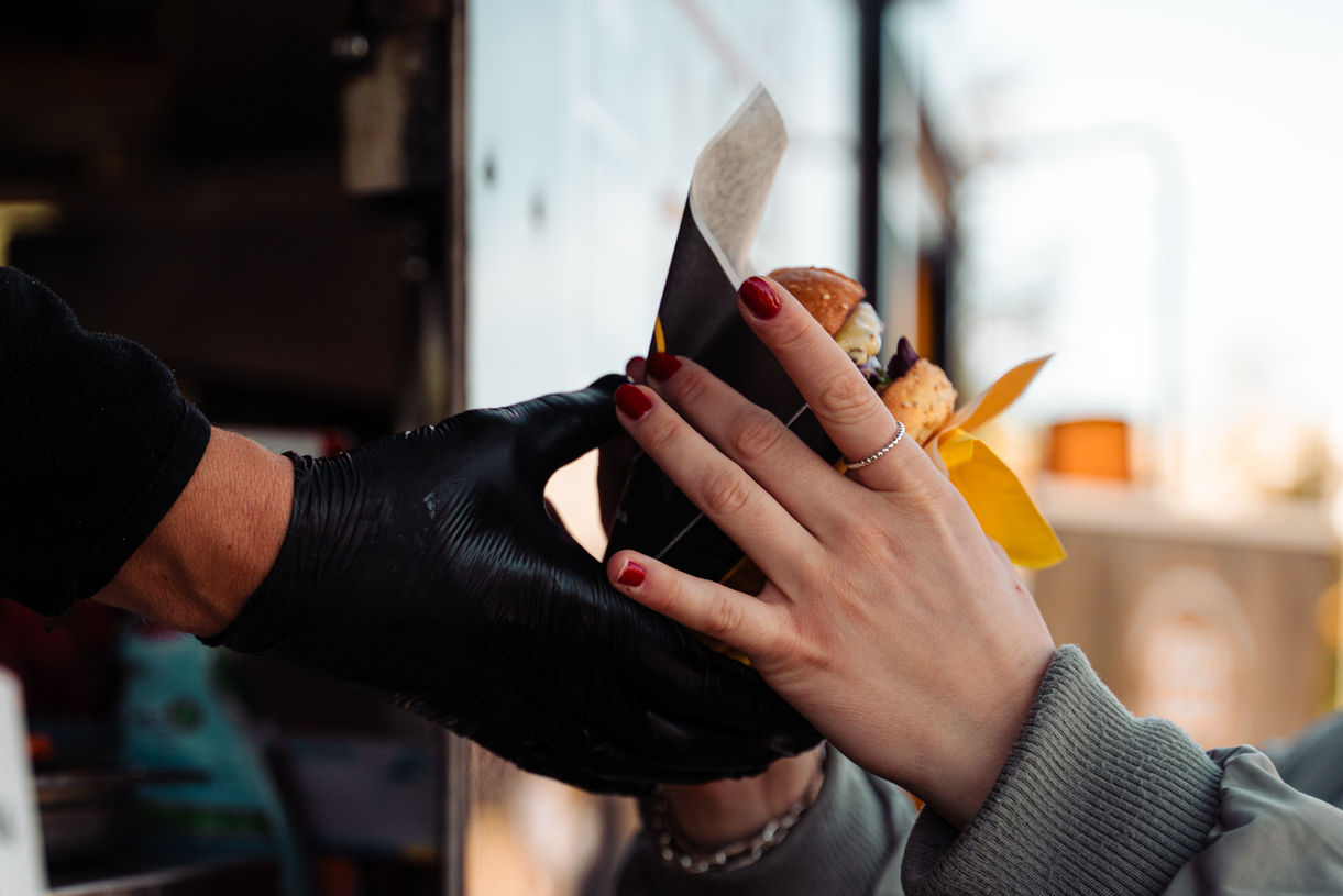 Hand übergibt einen Burger beim Bar Convent Berlin (BCB) 2024, Messe Berlin. Messefotografie mit kulinarischem Fokus.