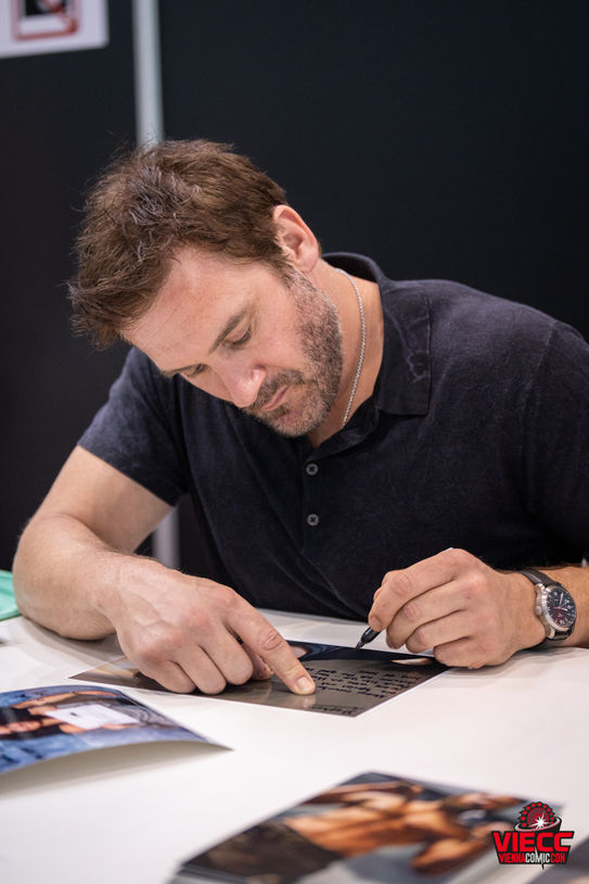 Schauspieler signiert Autogrammkarten und spricht mit Fans auf der Vienna Comic Con (VIECC). Persönliche Begegnung und direkte Interaktion.
