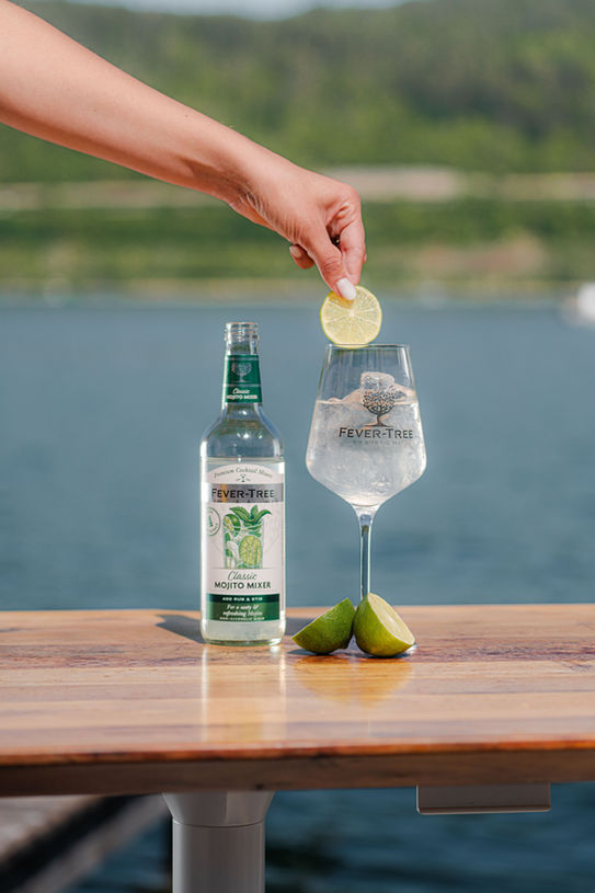Zitronenscheibe wird in ein Fever-Tree Glas gegeben. Content-Produktion am Wörthersee mit natürlicher Produktfotografie.