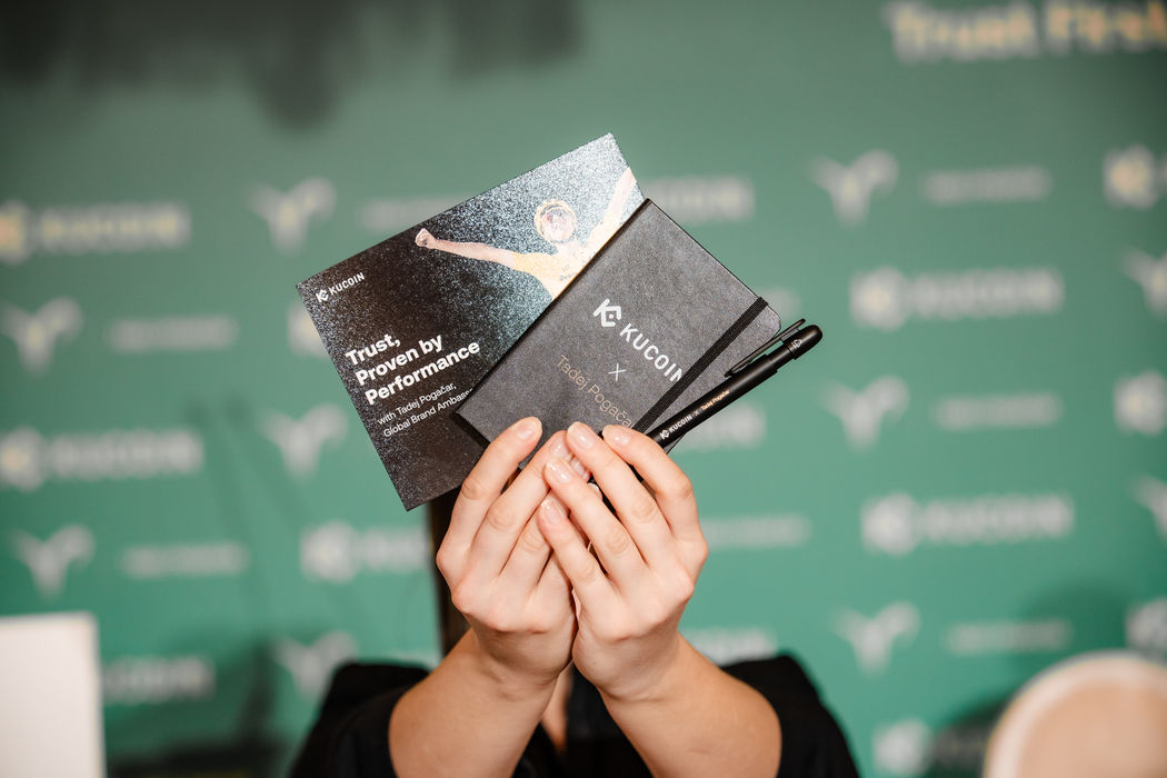 KuCoin-Pressematerial mit Notizbuch und Kugelschreiber mit Branding von KuCoin und Tadej Pogačar vor der Pressekonferenz im Hotel Sacher Wien. Event-Fotografie von FRB Media.